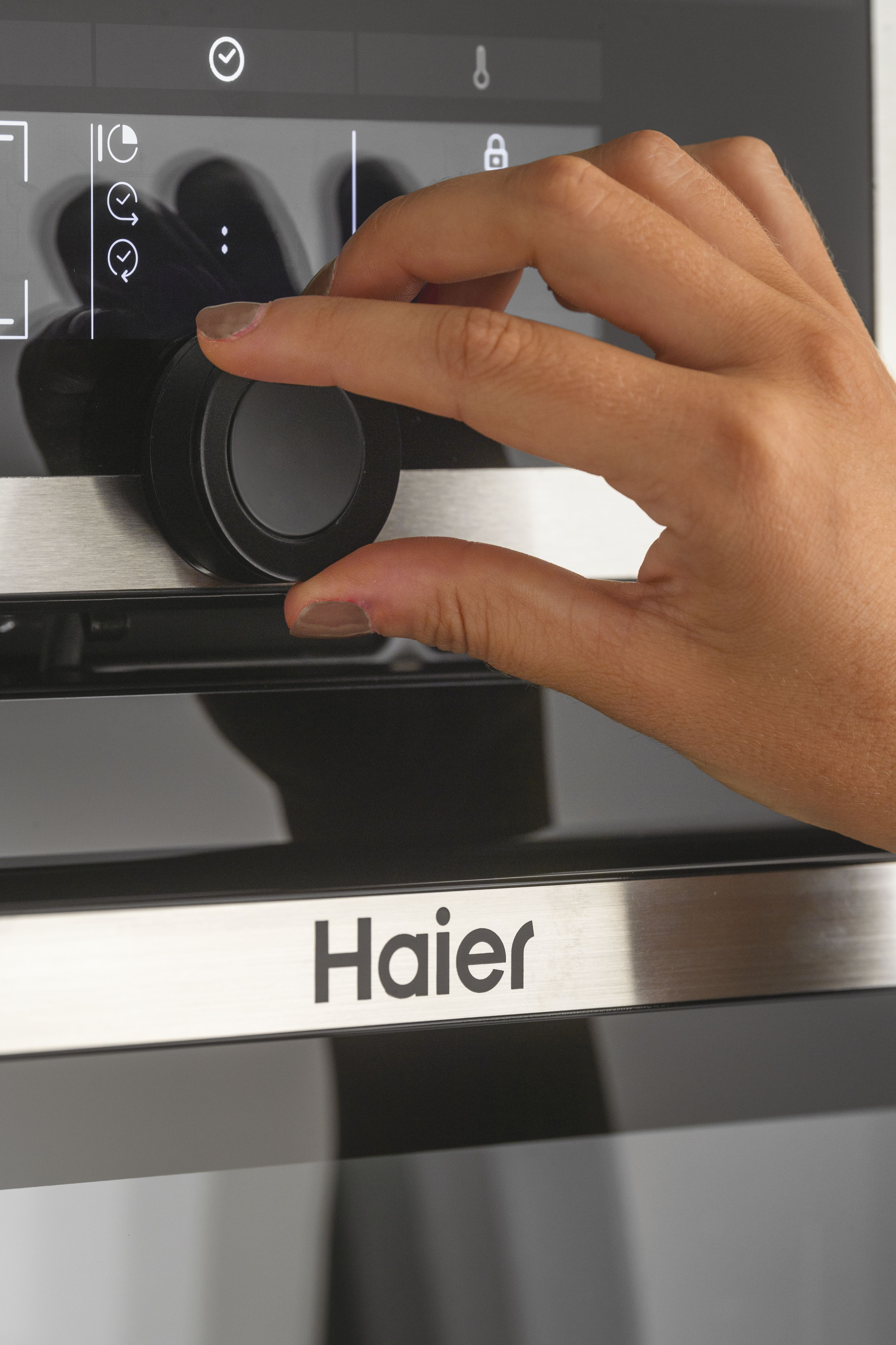 Una mano gira una manopola su un forno Haier. Lo schermo ha icone e il nome del marchio è visibile.