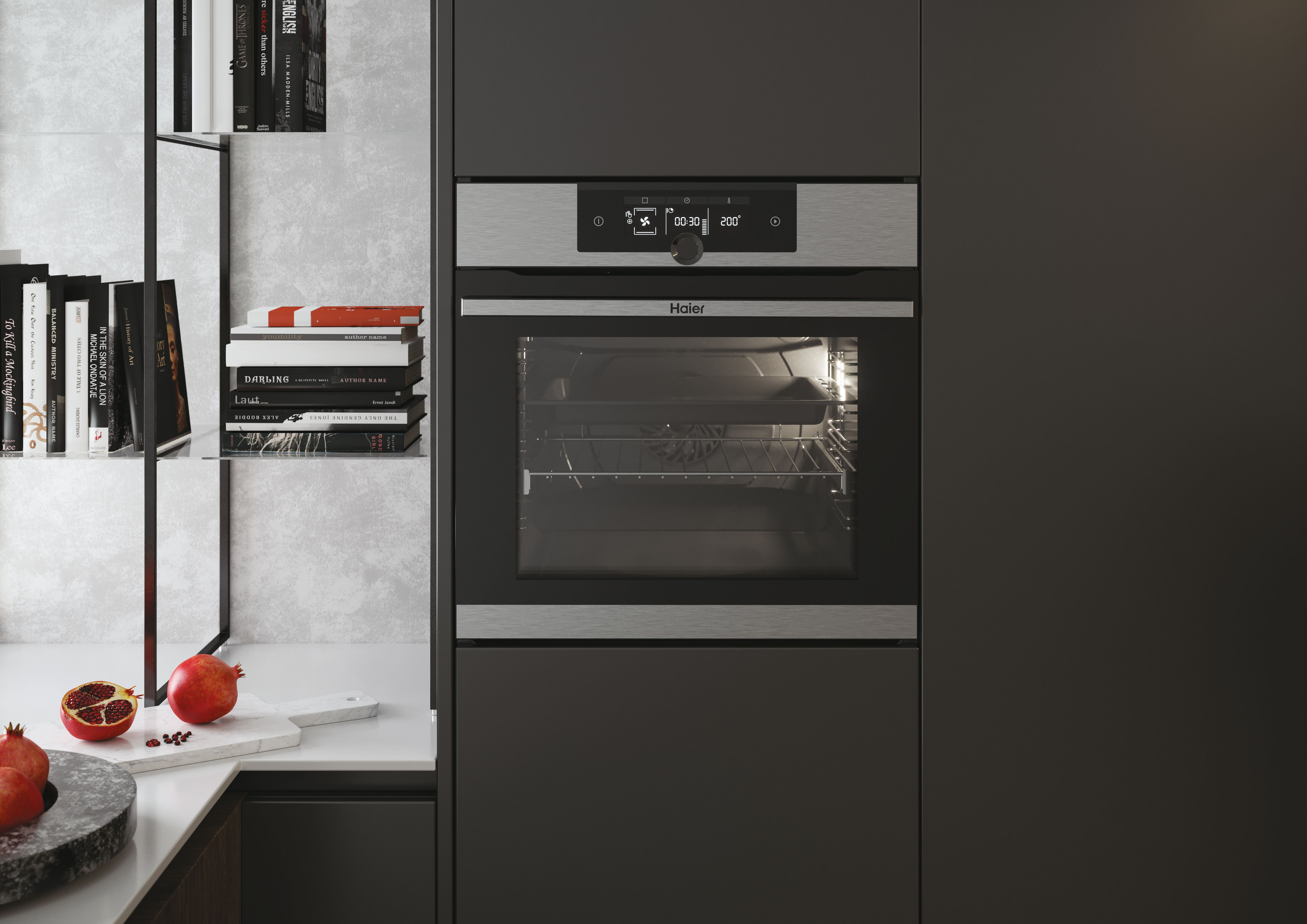 Forno con display digitale, libri su uno scaffale e melograni su superficie in marmo.