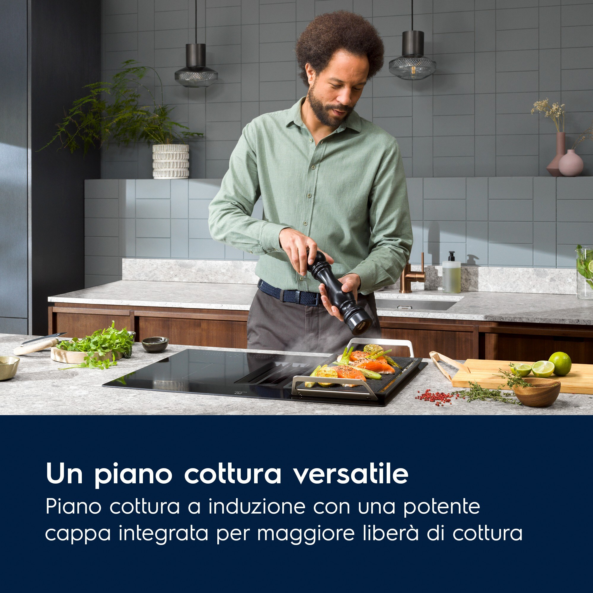 Uomo in cucina che condisce il cibo su un piano cottura. Salmone e asparagi visibili. Cucina con piastrelle e piani di lavoro grigi.
