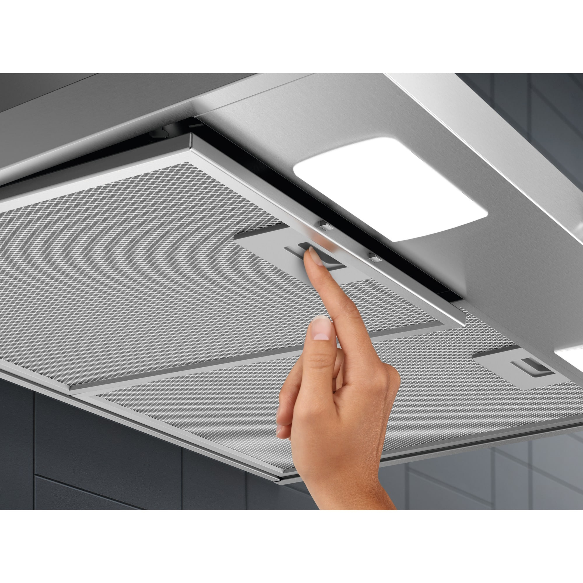 Ręka reguluje metalowy filtr okapu. Okap ma światło na górze i ciemnoszare tło.