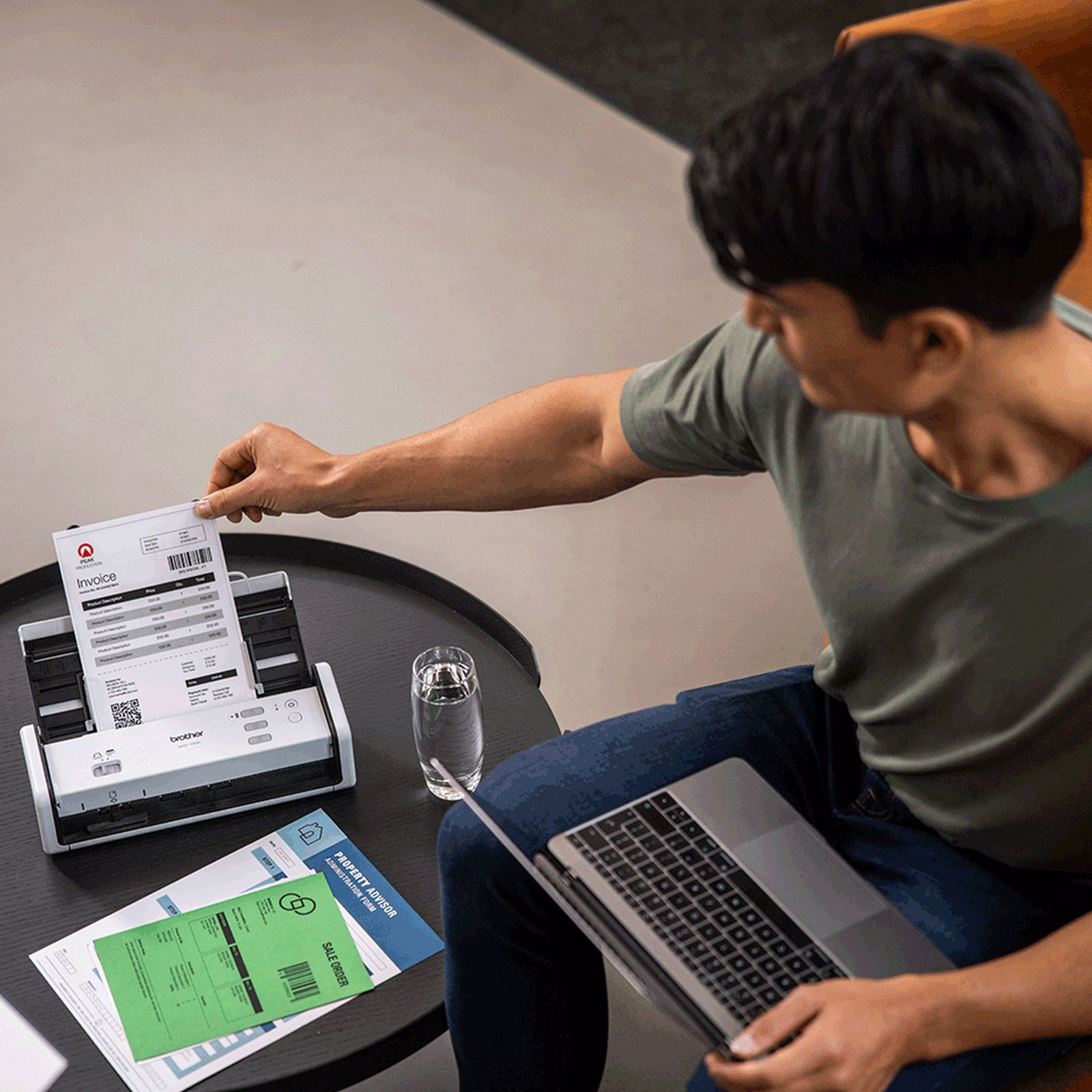 Mężczyzna skanuje fakturę skanerem Brother. Na stole laptop, szklanka wody i dokumenty.
