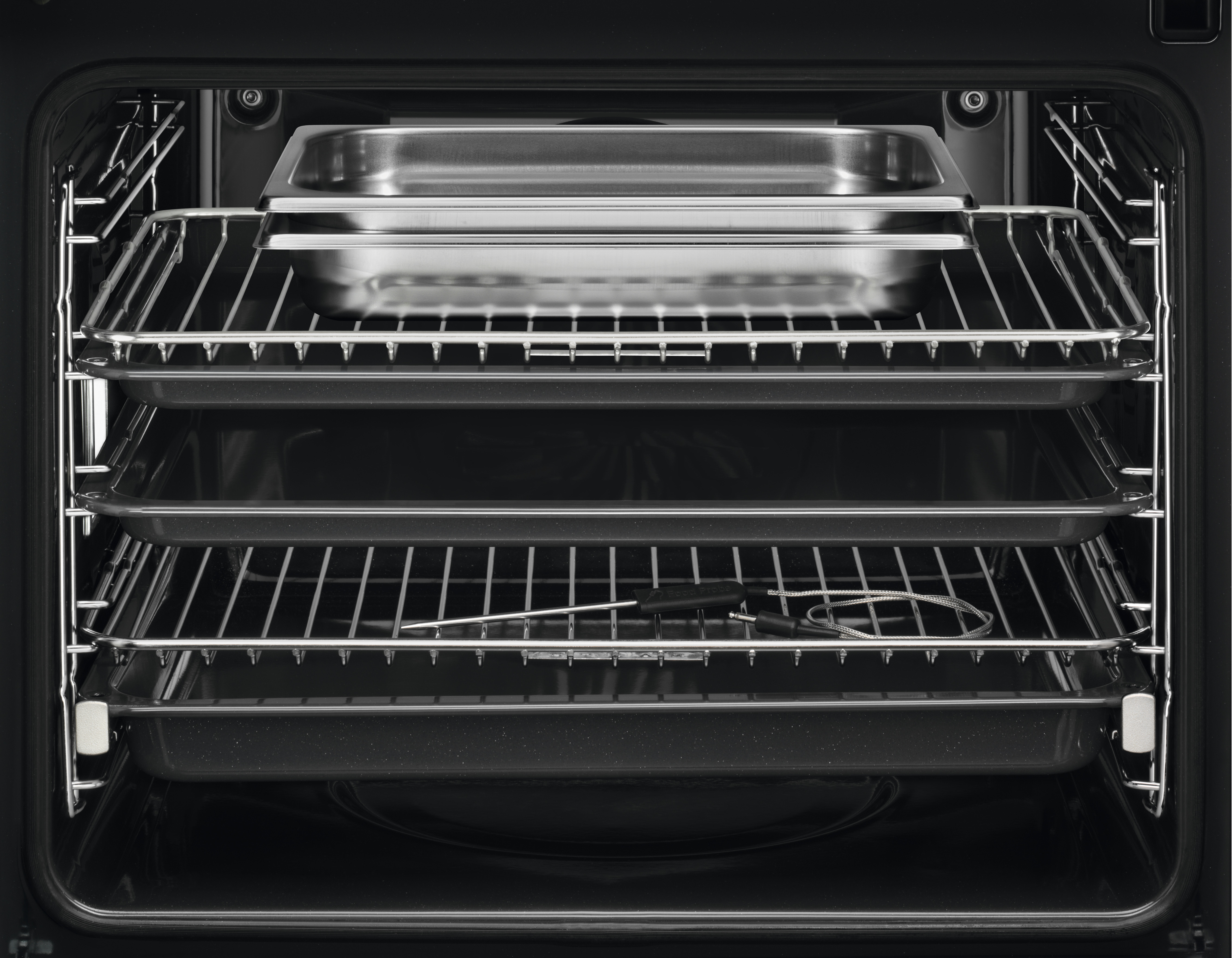Interno del forno con vassoi, griglie e sonda per alimenti. Padelle in acciaio inox visibili. Interno nero.
