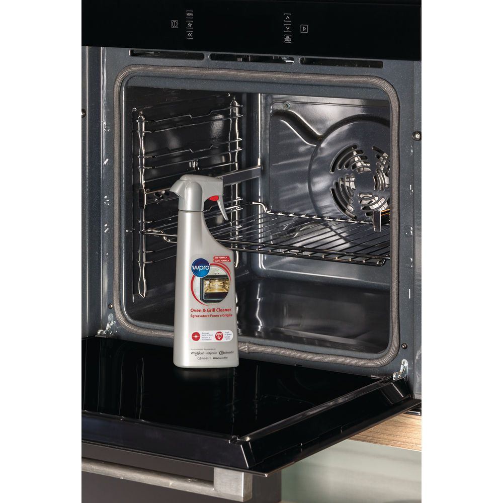 Interno di un forno con una bottiglia di detergente per forni. La porta del forno è aperta. Ci sono griglie e una ventola.