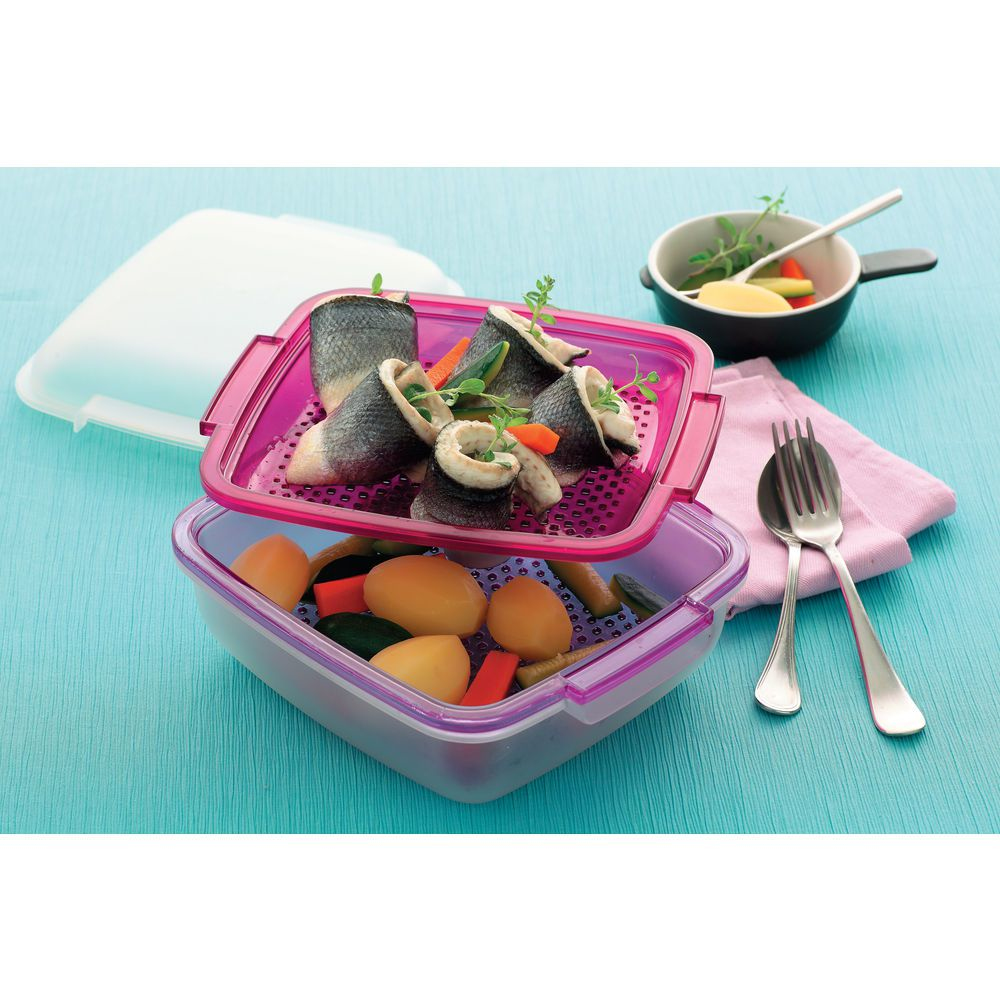 Un contenitore per alimenti con involtini di pesce e verdure. Una piccola padella con verdure e posate. Tutto su una superficie blu.