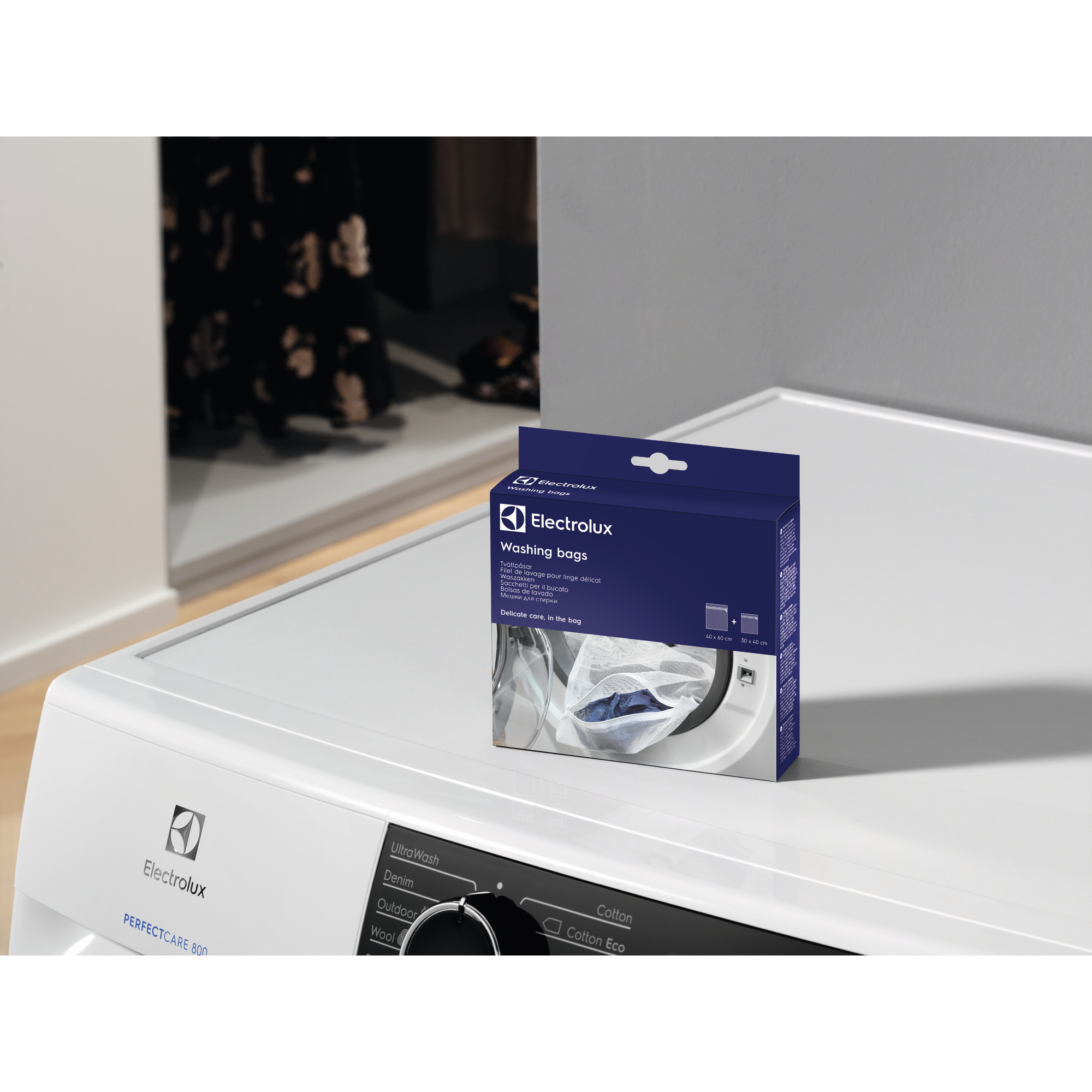 Una lavatrice con una scatola di sacchi per lavaggio Electrolux sopra. La scatola è blu con testo bianco e l'immagine di un sacco per lavaggio.