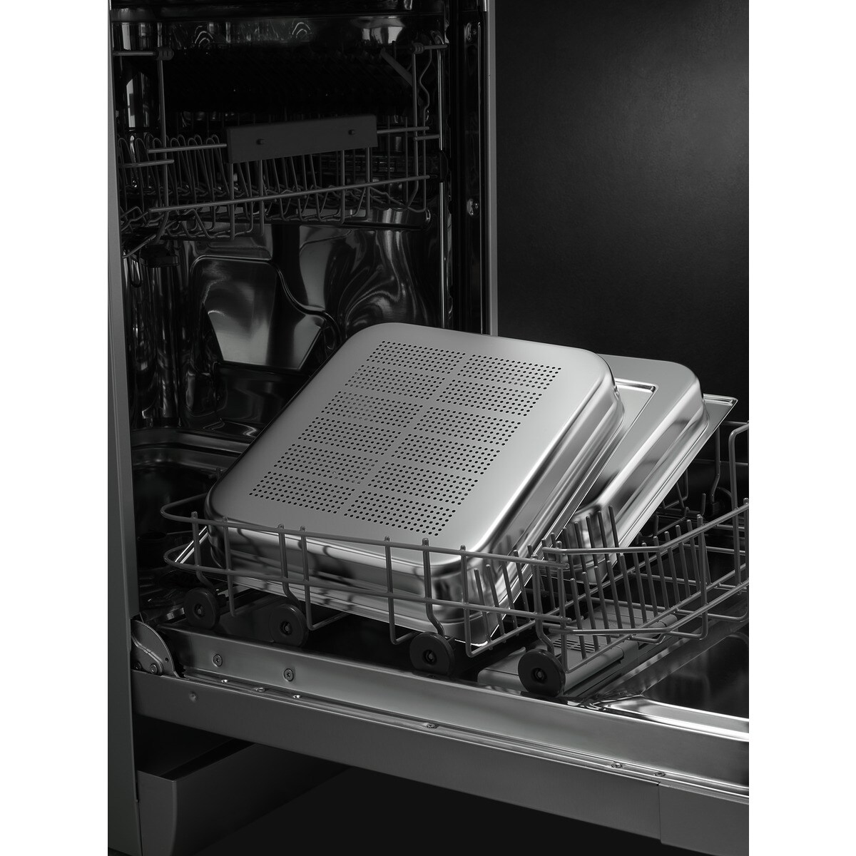 Innenraum eines Geschirrspülers mit Metalltabletts. Das obere Tablett hat einen perforierten Deckel. Die Tabletts befinden sich im unteren Rack.
