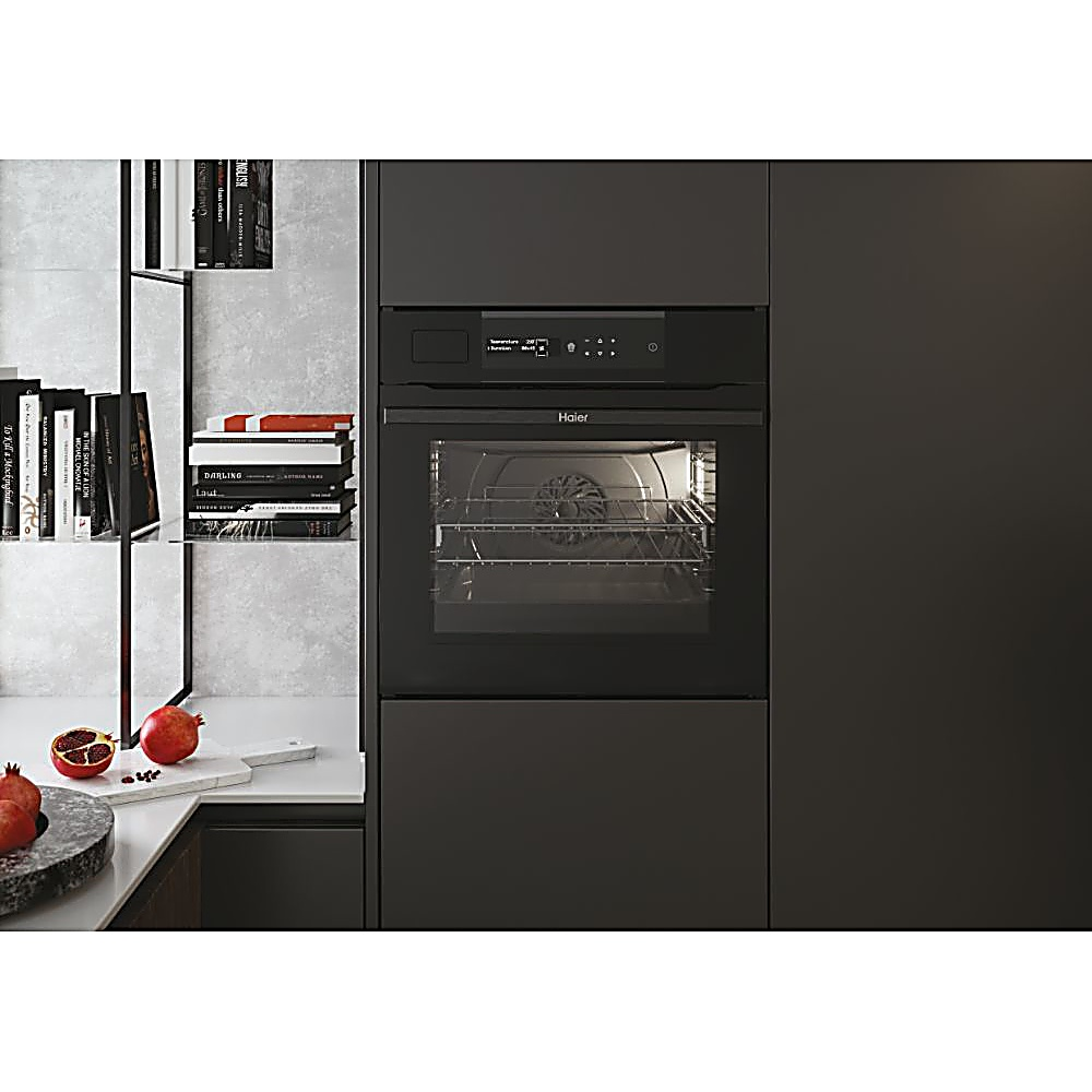 Una moderna cucina con forno nero e scaffale di libri. Melograni sul bancone. Il forno ha il logo Haier.