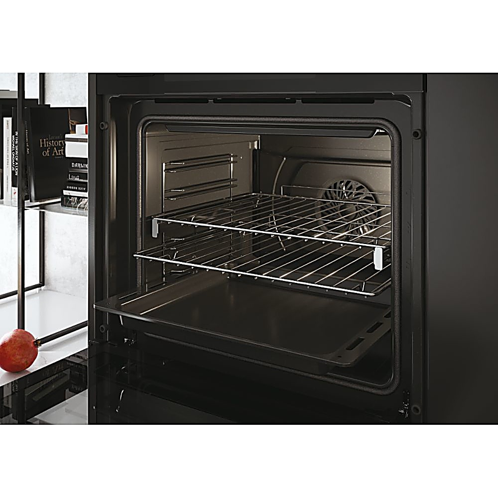 Un forno nero aperto con griglie e una teglia. Libri e un melograno sul lato sinistro.