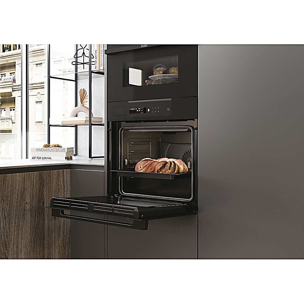Un moderno forno nero con pane all'interno. Sopra c'è un microonde. Libri e una finestra sullo sfondo.