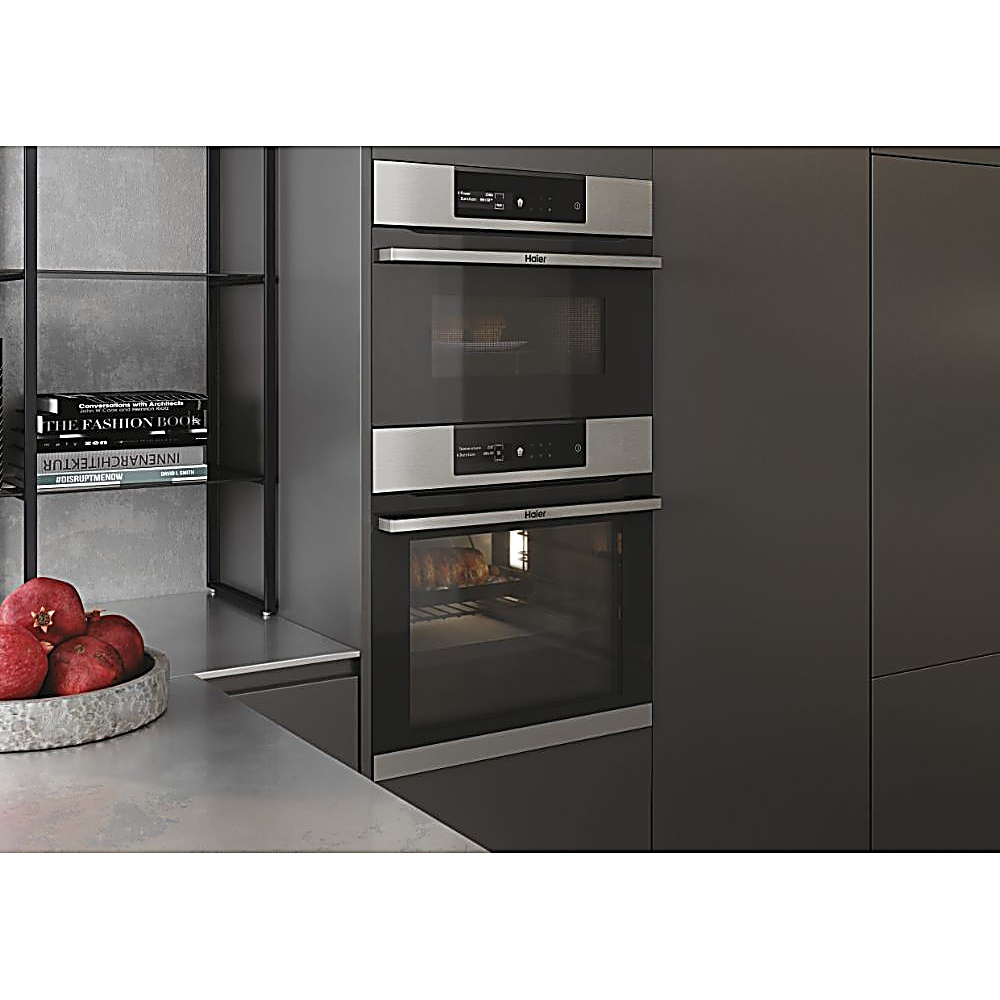 Una cucina moderna con forno e microonde Haier integrati. Una mensola con libri e una ciotola di melograni sono sul bancone.