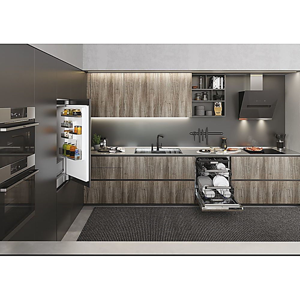 Cucina moderna con frigorifero aperto, lavastoviglie, armadi in legno e piano di lavoro nero. Tappeto grigio sul pavimento.