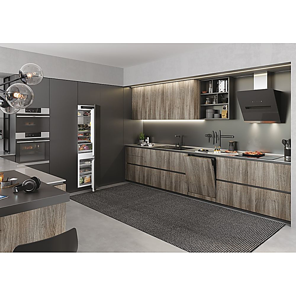 Cucina moderna con mobili in legno, frigorifero e piano di lavoro nero. C'è un tappeto scuro sul pavimento.