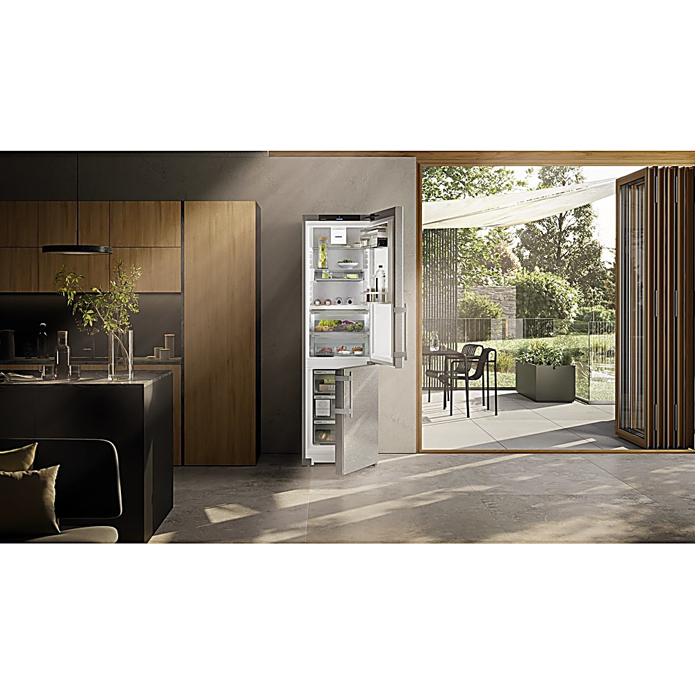 Una cocina moderna con refrigerador abierto, puertas a un patio con muebles y vista al jardín.