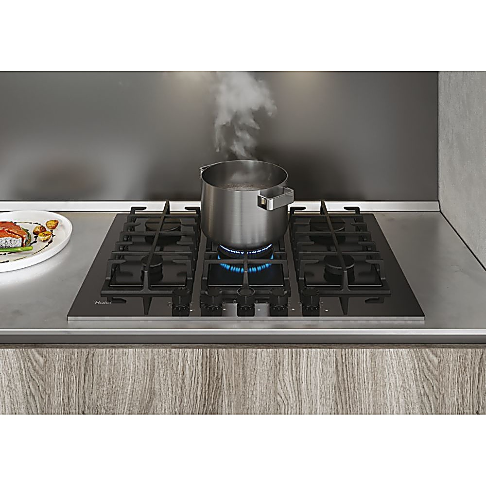 Płyta kuchenna z garnkiem wrzącej wody i parą. Talerz z jedzeniem po lewej stronie. Tło to szara powierzchnia.