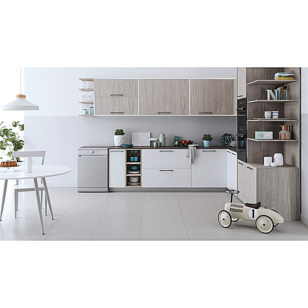 Cucina moderna con mobili bianchi e in legno, elettrodomestici in acciaio inox e un'auto giocattolo. Tavolo rotondo e sedie.