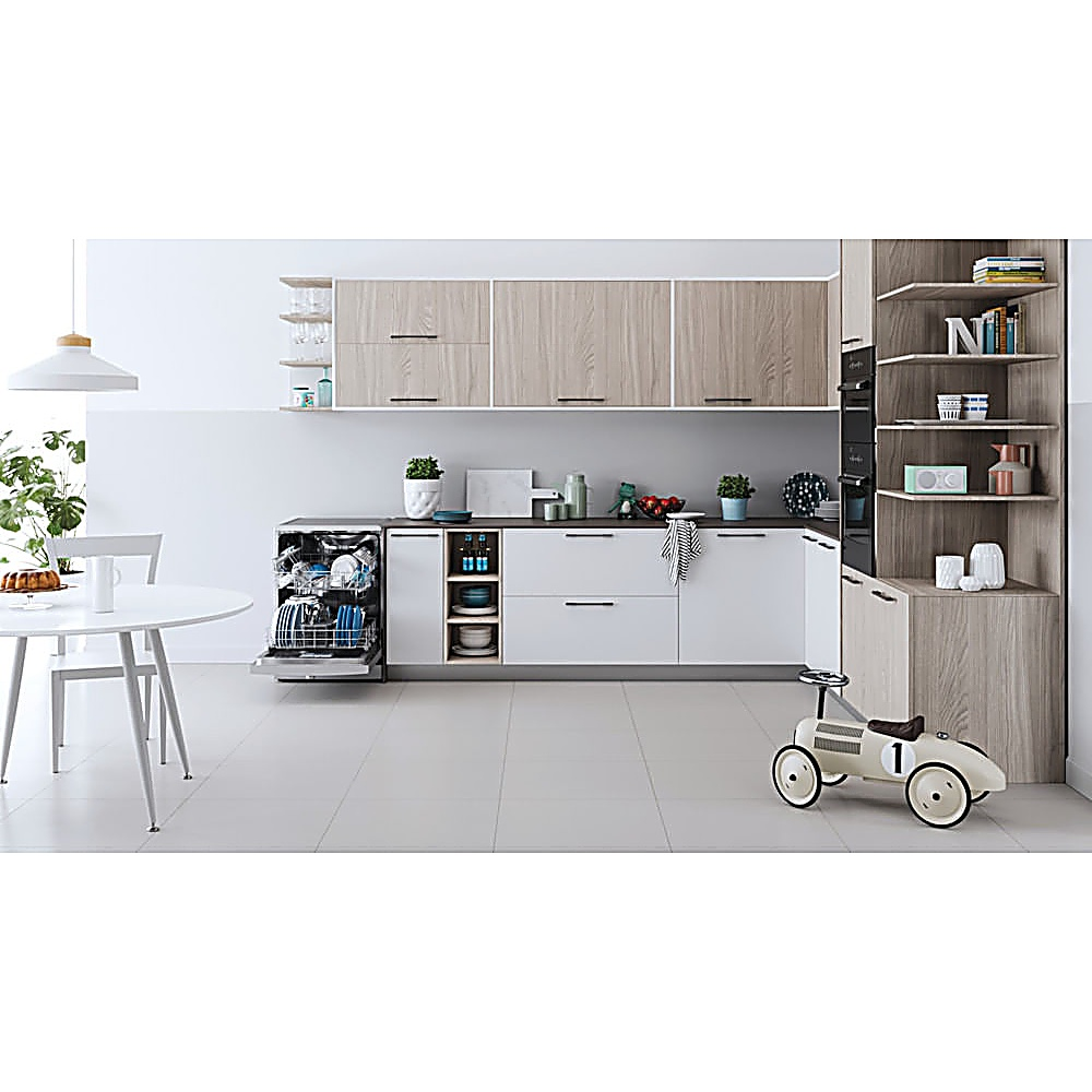 Cucina moderna con mobili bianchi, lavastoviglie aperta, dettagli in legno e un'auto giocattolo. Tavolo rotondo con torta.