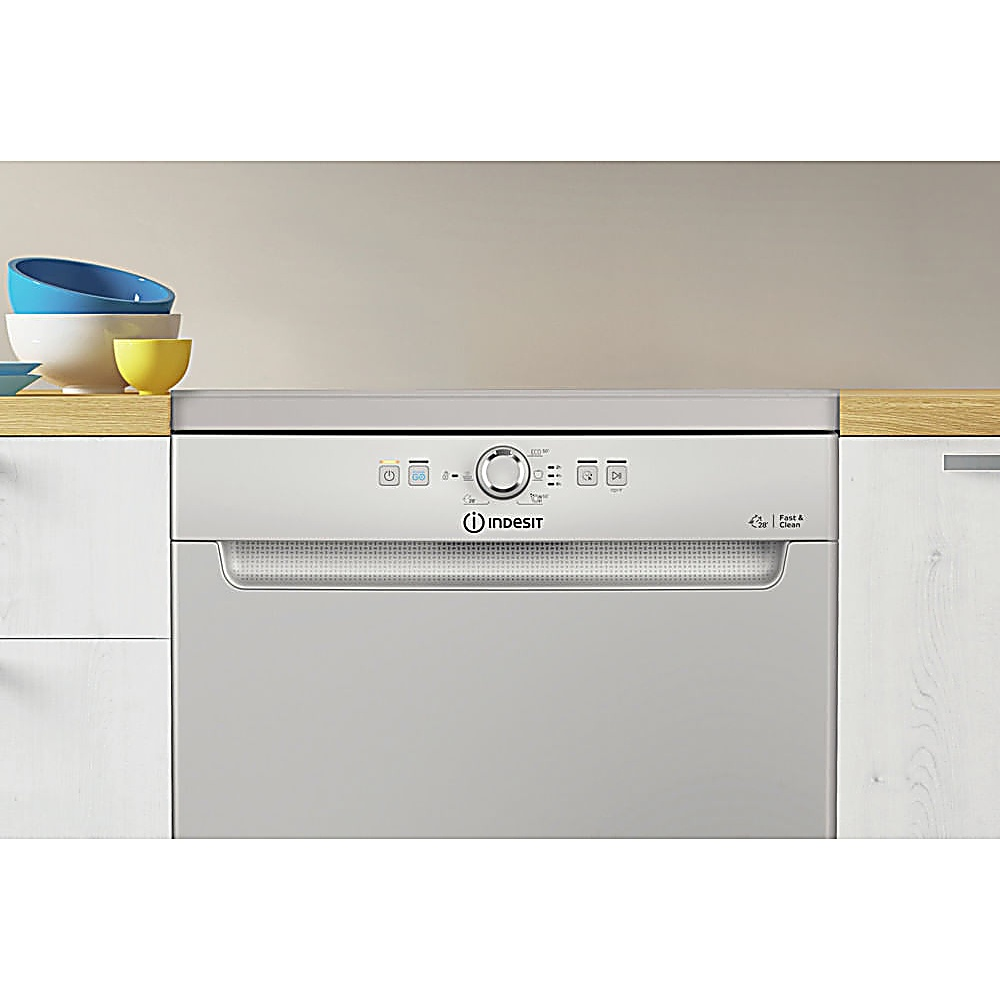 Una lavastoviglie Indesit grigia con pulsanti di controllo. Ciotole sul bancone. Lo sfondo è beige chiaro.