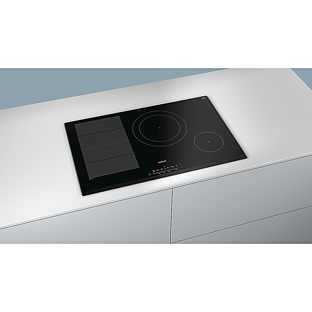 Un piano cottura a induzione Siemens nero con tre fuochi e un pannello di controllo è appoggiato su un piano bianco. Lo sfondo è grigio chiaro.