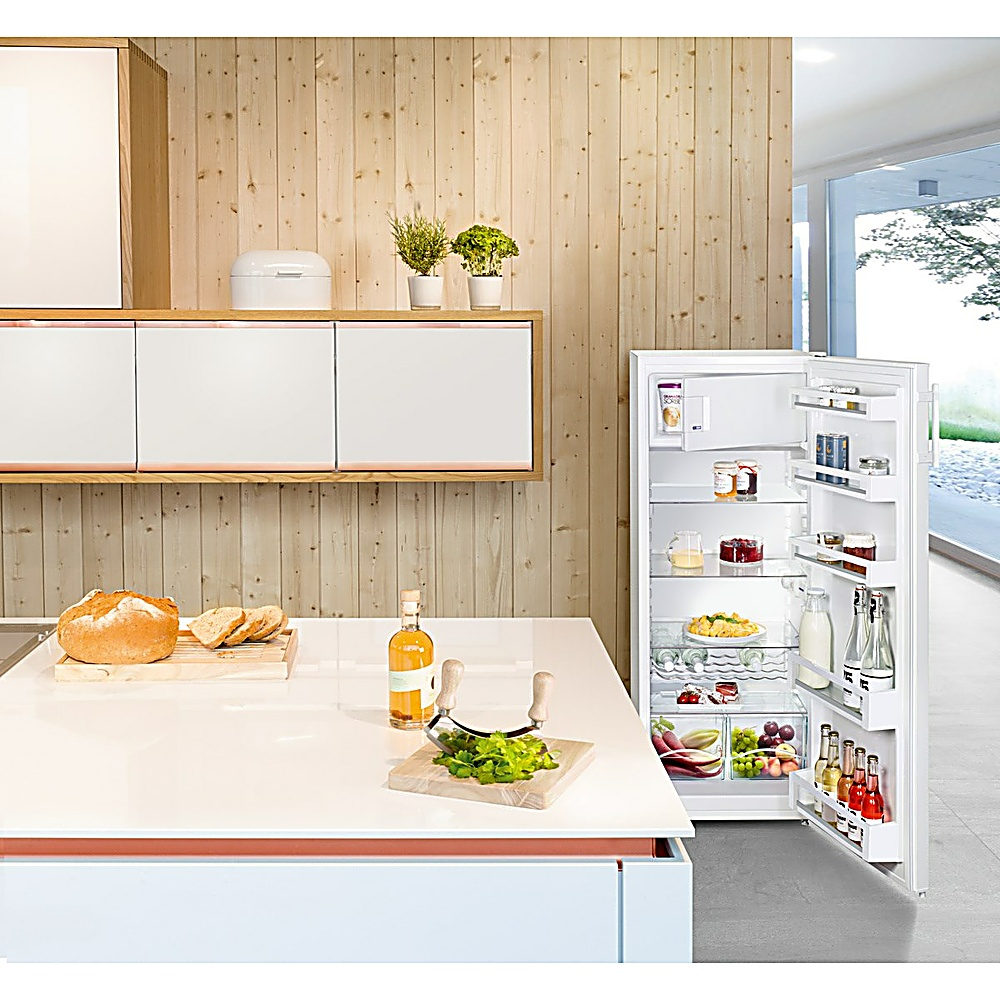 Una scena di cucina con frigorifero aperto, pane e tagliere. All'interno del frigorifero ci sono generi alimentari. Parete in legno e armadi bianchi.