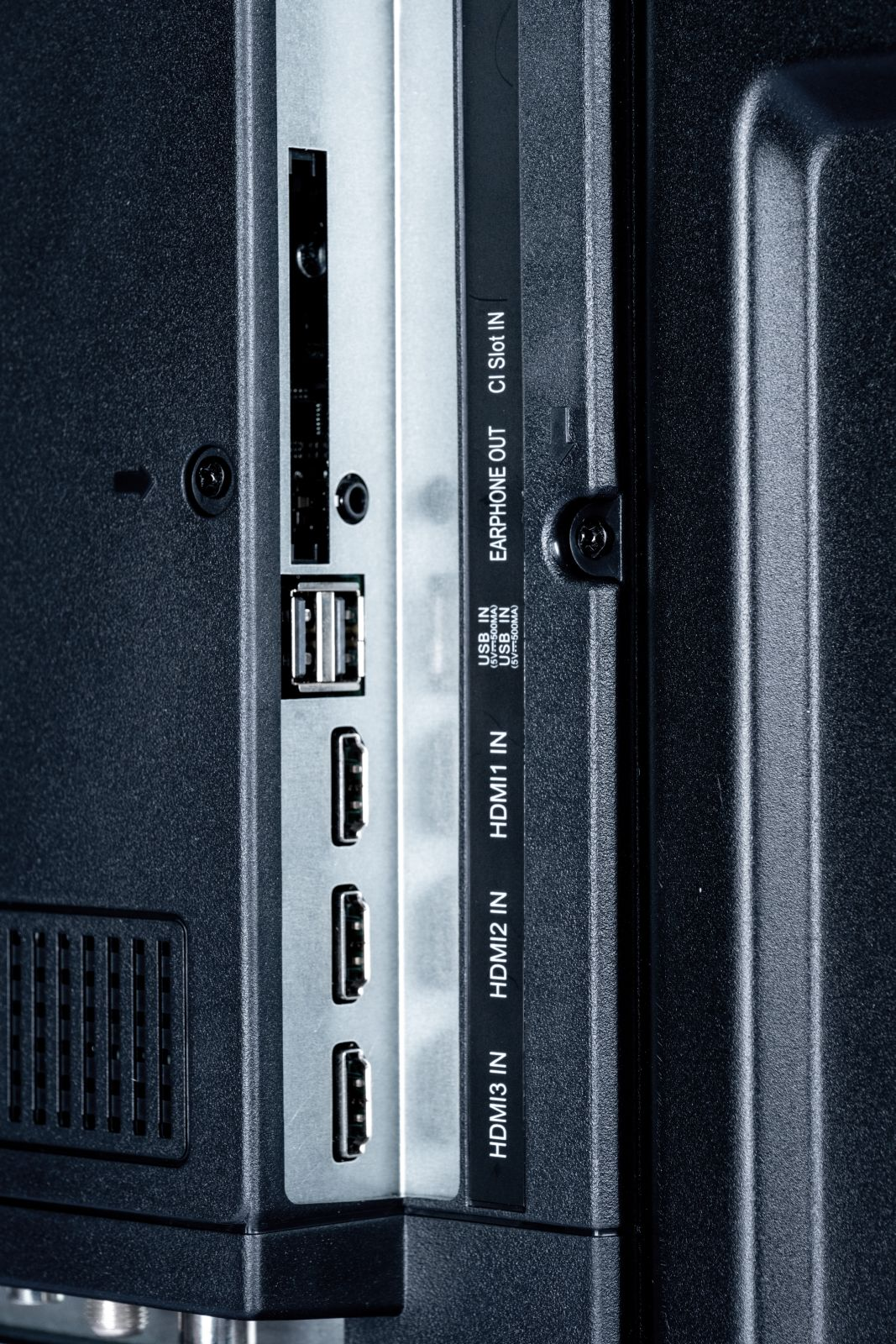 Zbliżenie tylnego panelu telewizora. Widoczne porty USB, HDMI, wyjście słuchawkowe i gniazdo CI. Panel jest czarny ze srebrnymi akcentami.