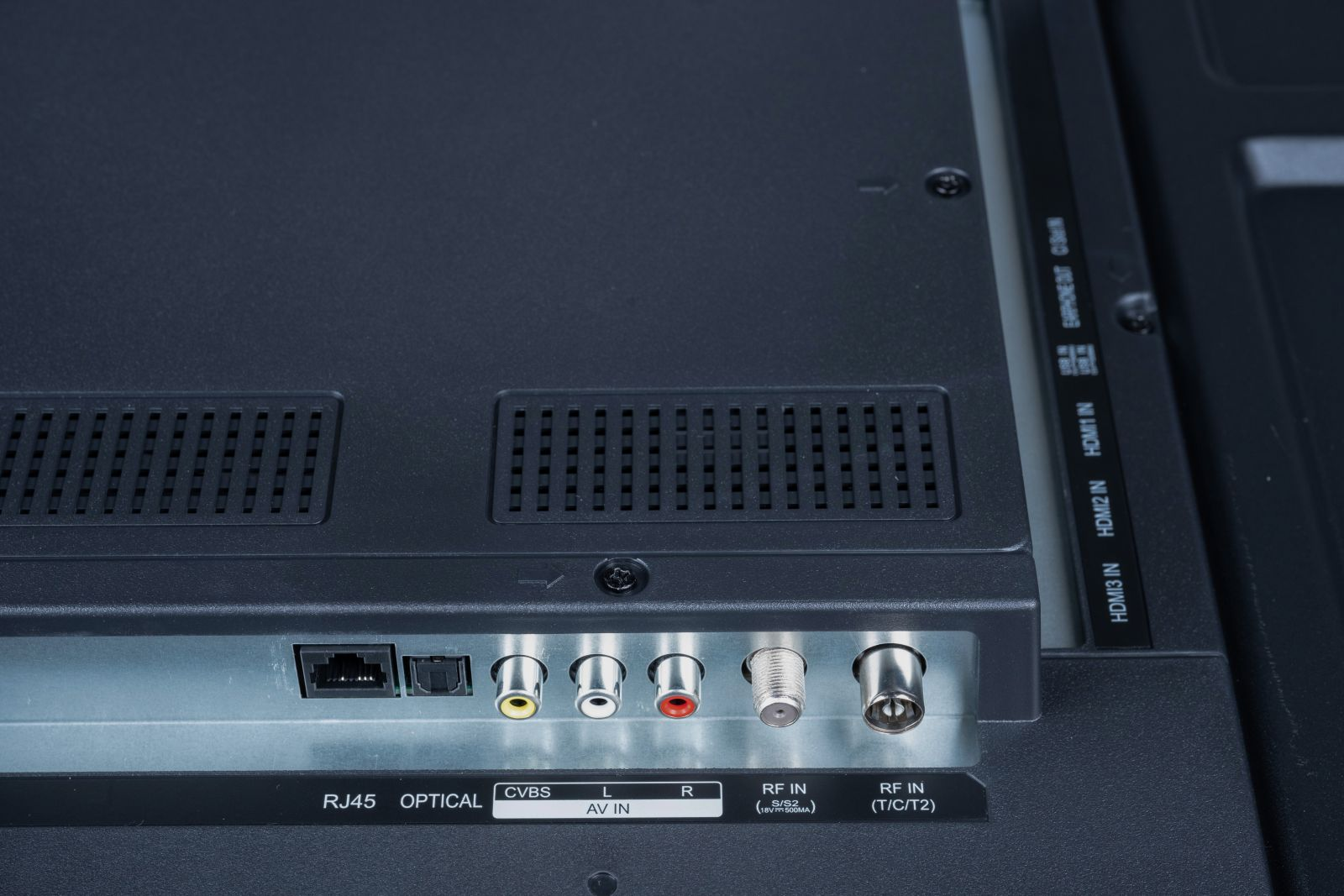 Zbliżenie tylnego panelu telewizora z różnymi portami wejściowymi, w tym HDMI, RJ45 i AV. Panel jest czarny.