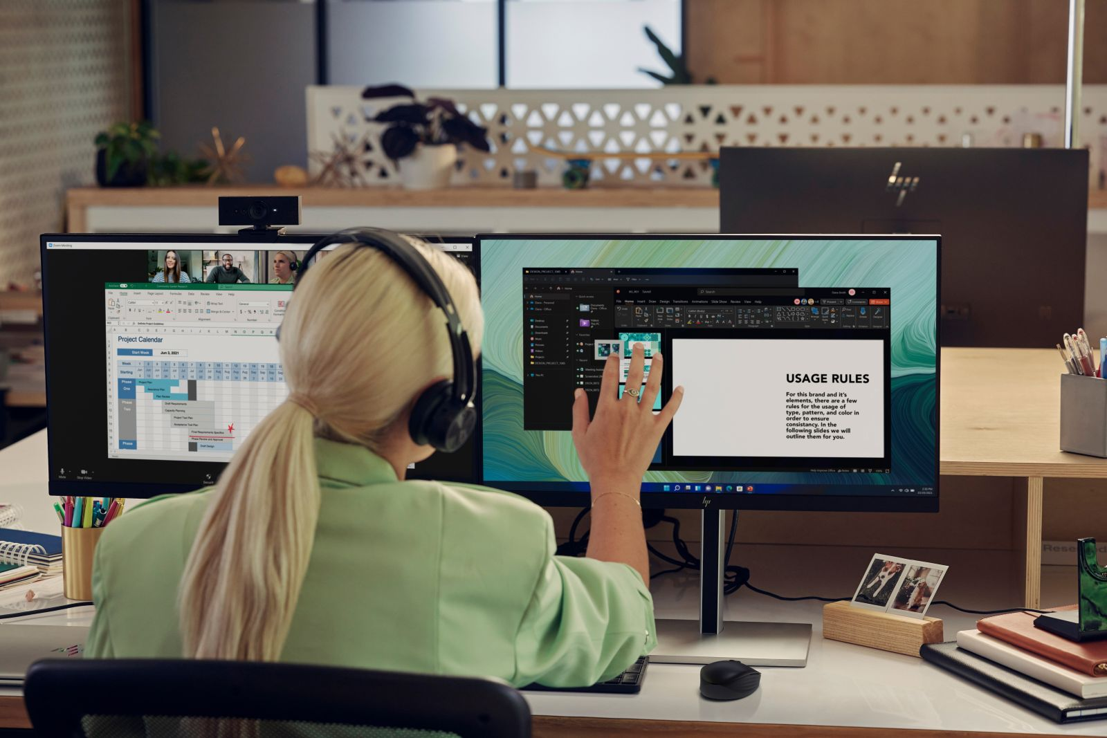 Eine Frau mit blonden Haaren und Kopfhörern arbeitet an einem Computer mit zwei Monitoren. Einer zeigt einen Kalender, der andere eine Präsentation.