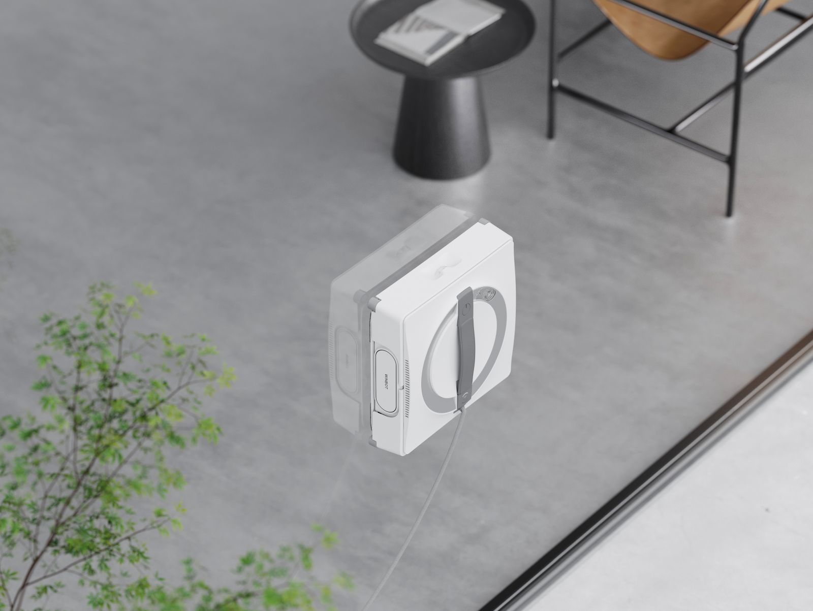 Biały robot do czyszczenia okien z szarym uchwytem na szybie. W tle stół, krzesło i drzewo.