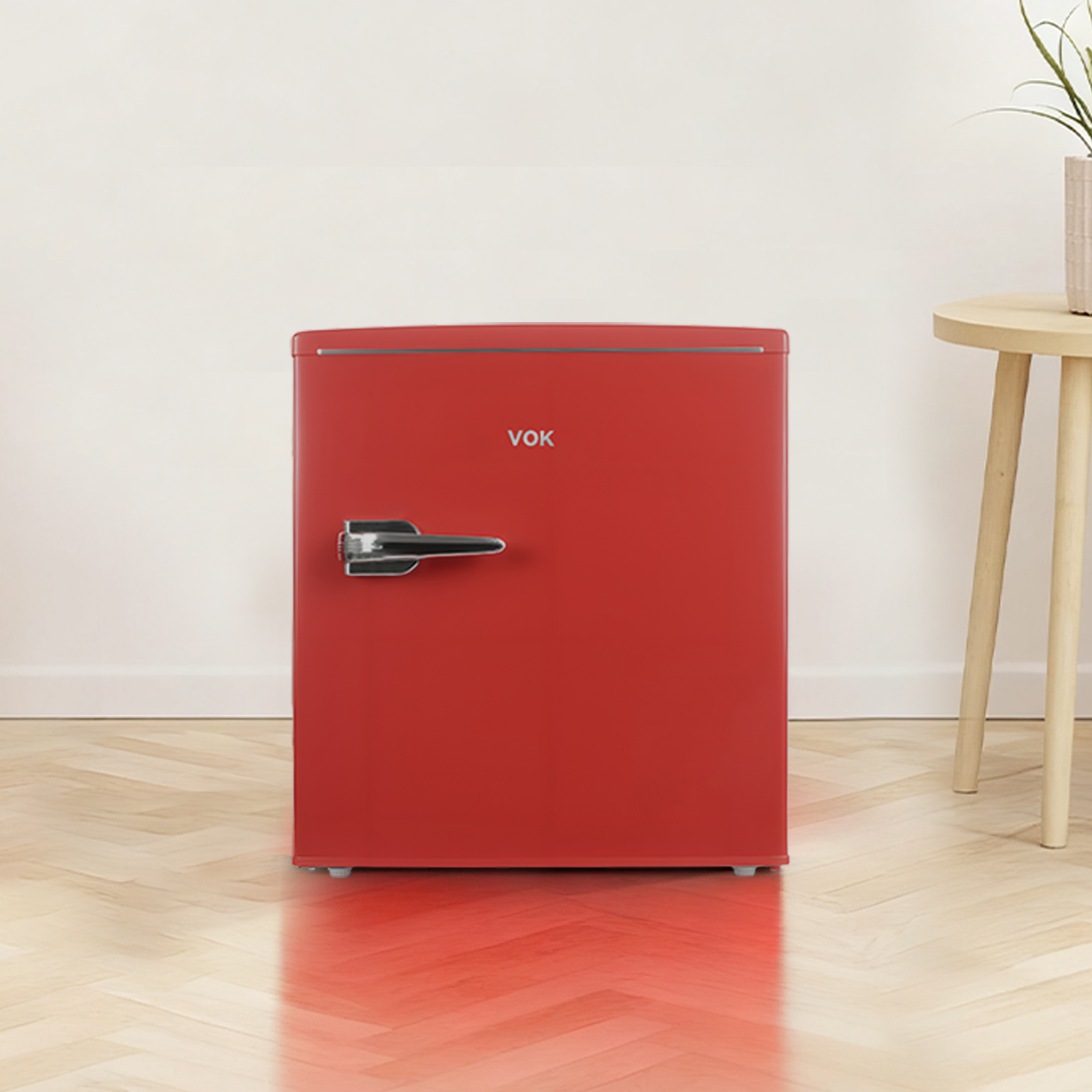 Un mini-refrigerador rojo con asa plateada. El refrigerador está frente a una pared blanca, junto a una mesa pequeña.