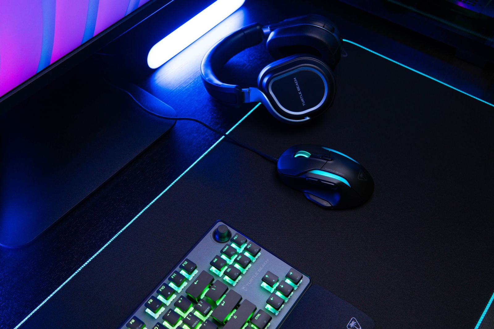 Konfiguracja do gier ze słuchawkami, myszką i klawiaturą. Klawiatura i mysz są podświetlane zielonym i niebieskim światłem.