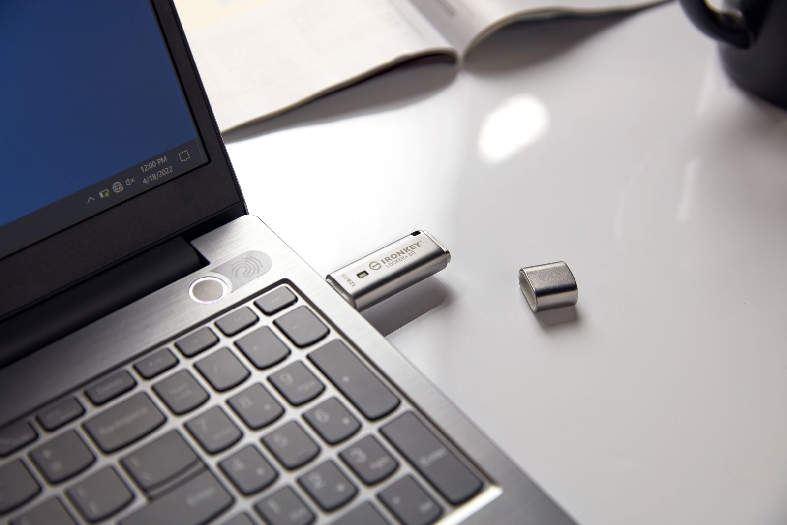 Laptop z włożonym pendrivem. Odkręcona nasadka obok napędu. Notatnik i kubek do kawy w tle.