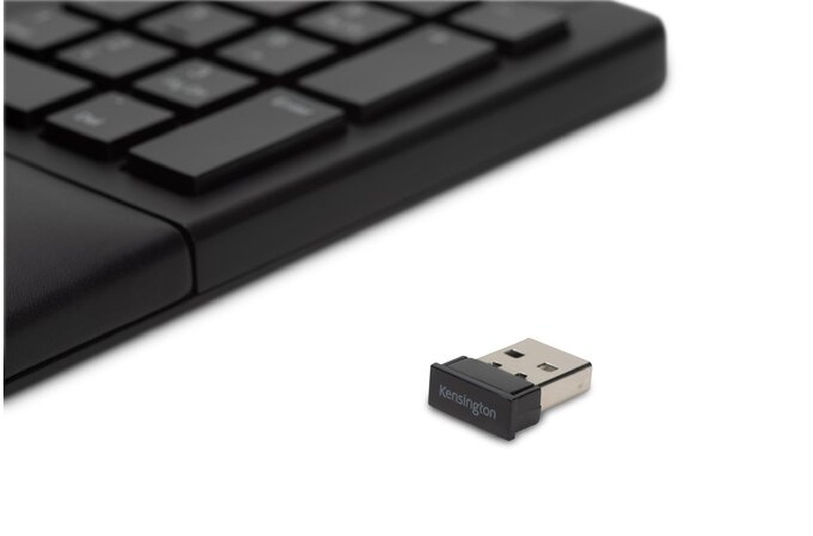 Teclado negro y receptor USB. El receptor está etiquetado como 'Kensington'. Fondo blanco.