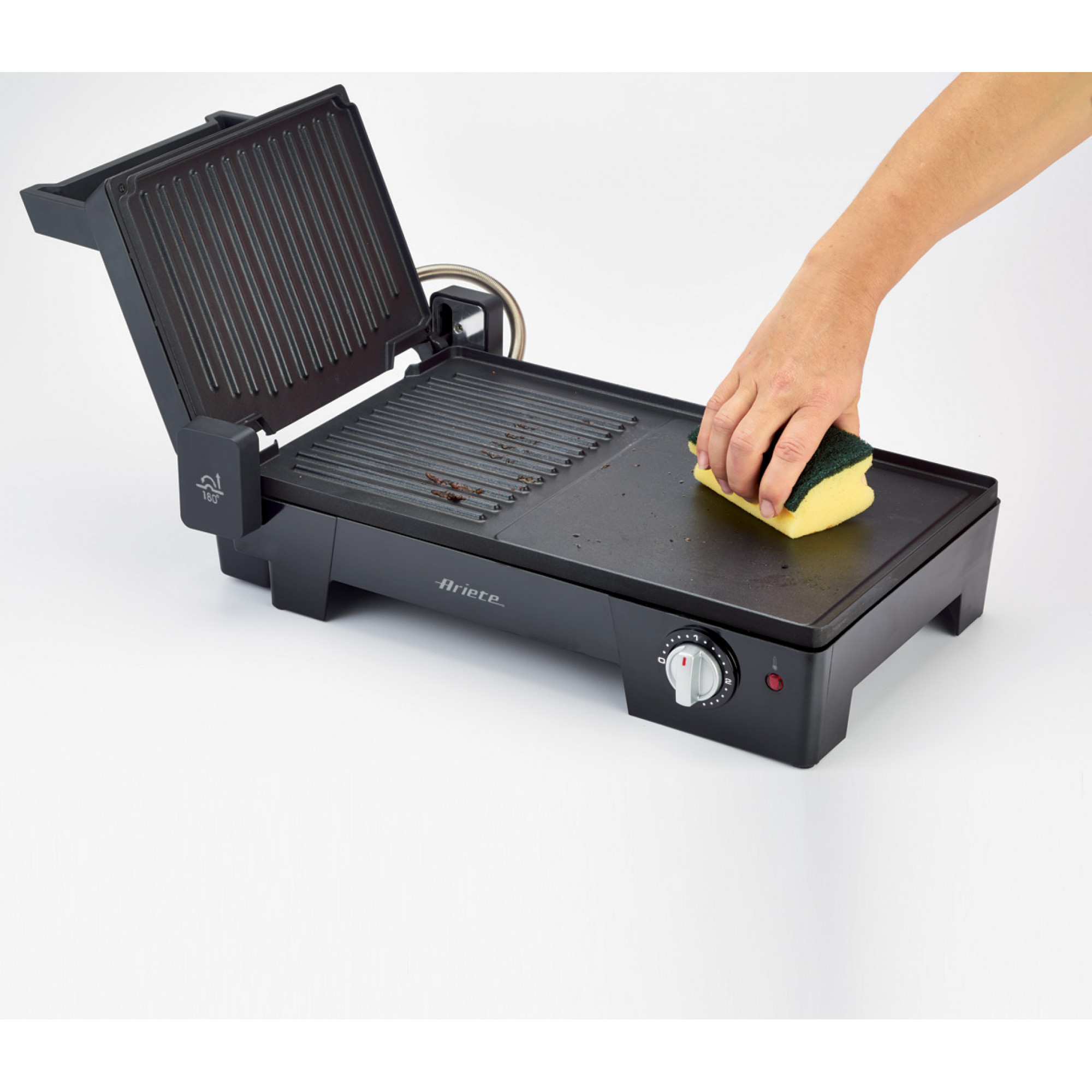 A black grill with the lid open. A hand cleans the grill with a yellow sponge.
