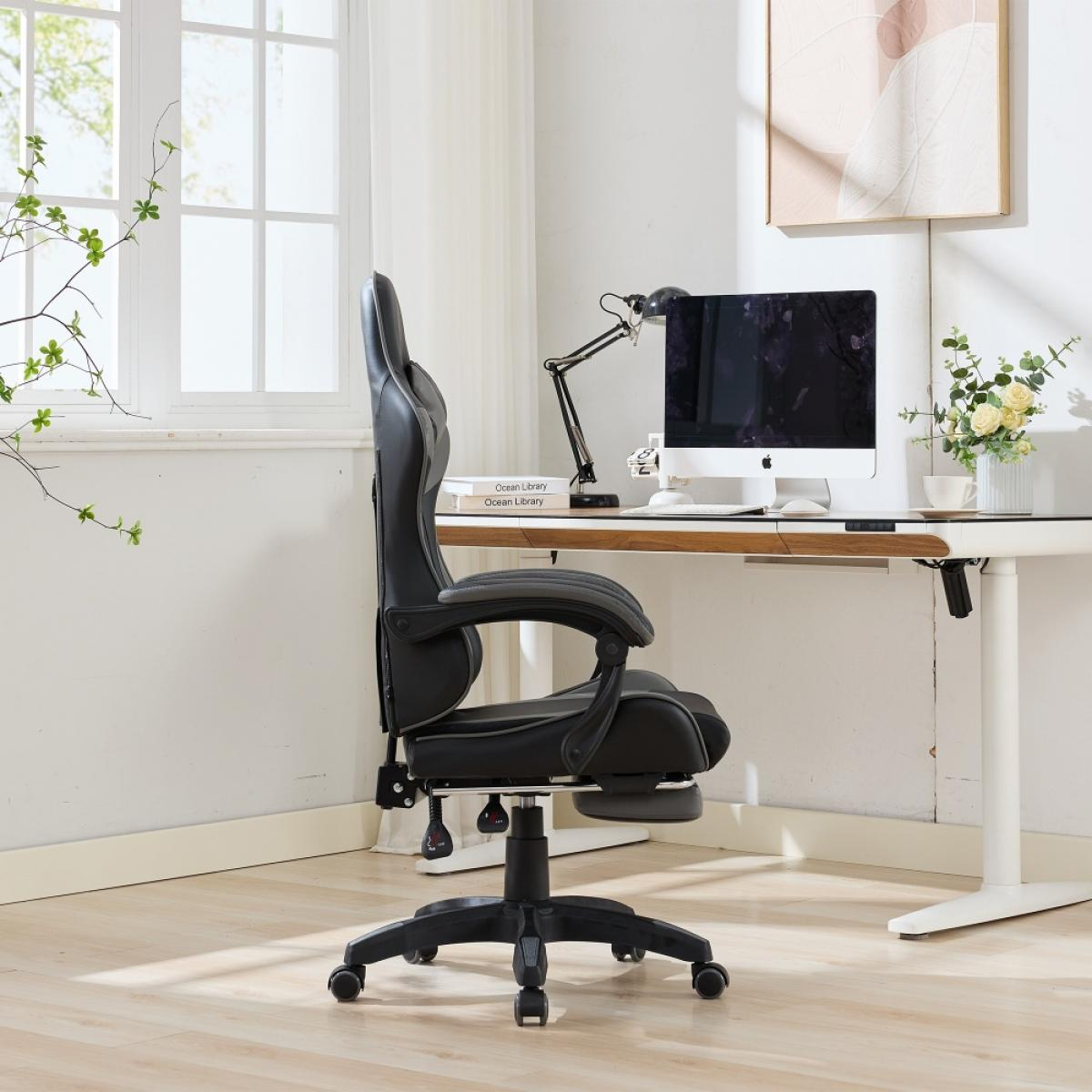 Ein schwarzer Gaming-Stuhl steht in einem Büro. Im Hintergrund ein Schreibtisch mit Computer und Lampe. Links ein Fenster.
