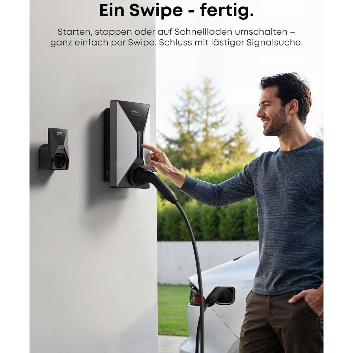 Ein Mann berührt eine Ladestation. Ein Auto ist angeschlossen. Die Station befindet sich an einer weißen Wand. Der Hintergrund zeigt Bäume und Himmel.
