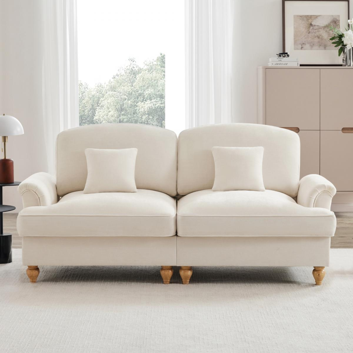 Ein cremefarbenes Sofa mit zwei Kissen steht auf einem weißen Teppich. Hinter dem Sofa befindet sich ein Fenster mit transparenten Vorhängen.