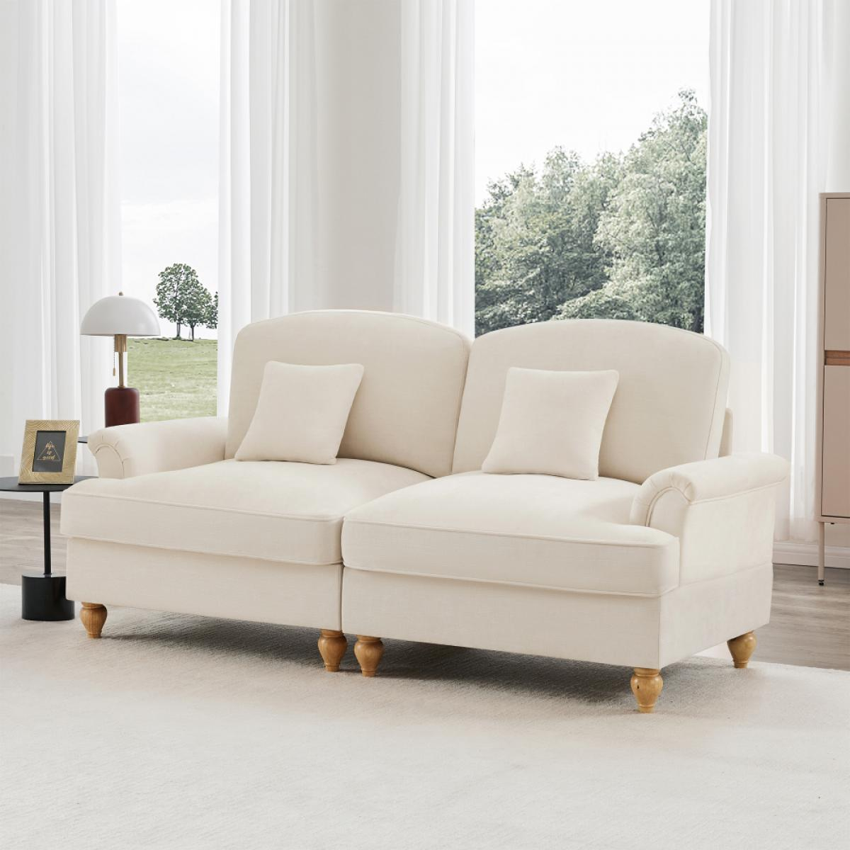 Cremefarbenes Sofa mit zwei Kissen, auf einem weißen Teppich. Dahinter ein Fenster mit transparenten Vorhängen und Blick auf Bäume.