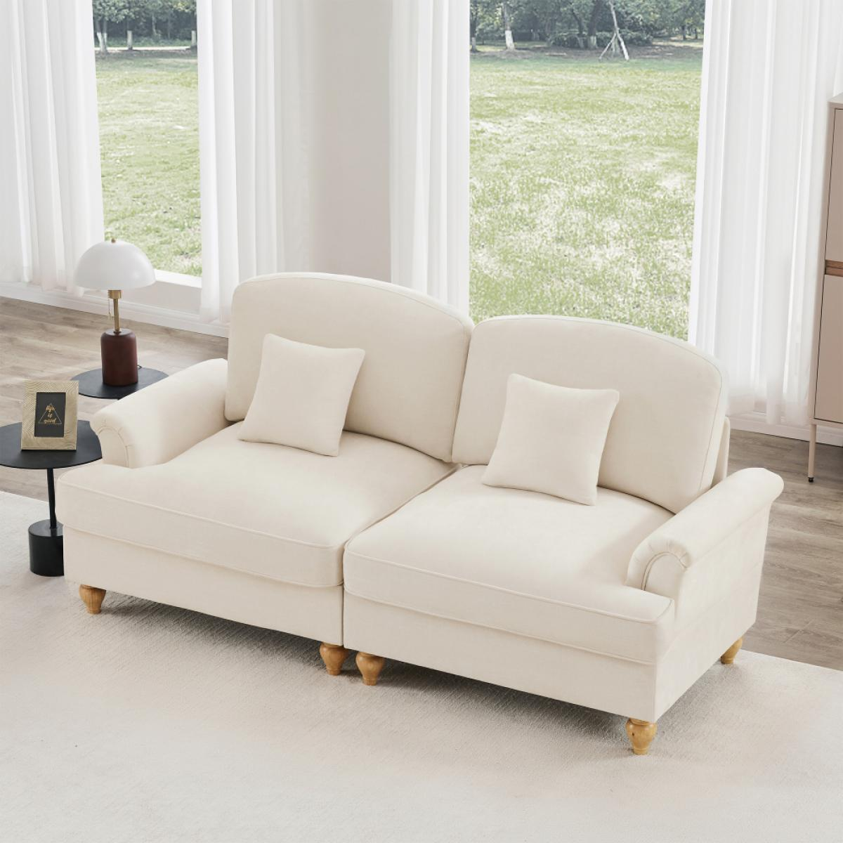 Cremefarbenes Sofa mit zwei Kissen auf weißem Teppich. Fenster mit weißen Vorhängen und Blick auf eine Grünfläche.