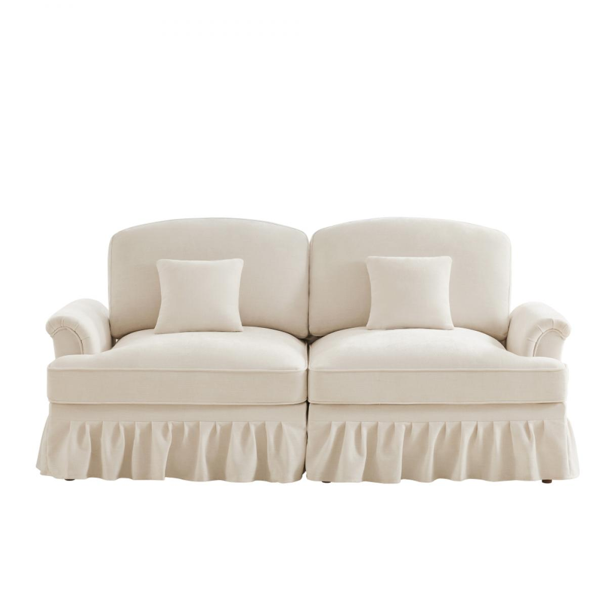 Cremefarbenes Sofa mit zwei Abschnitten, jeweils mit einem Kissen. Es hat einen gerüschten Rock und geschwungene Arme, vor weißem Hintergrund.