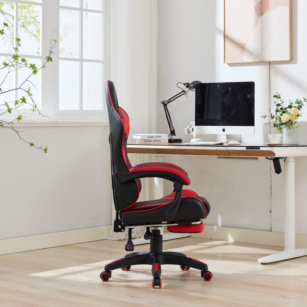Ein Gaming-Stuhl mit rotem und schwarzem Design. Daneben ein Schreibtisch mit Computer, Lampe und Blumen. Fenster im Hintergrund.