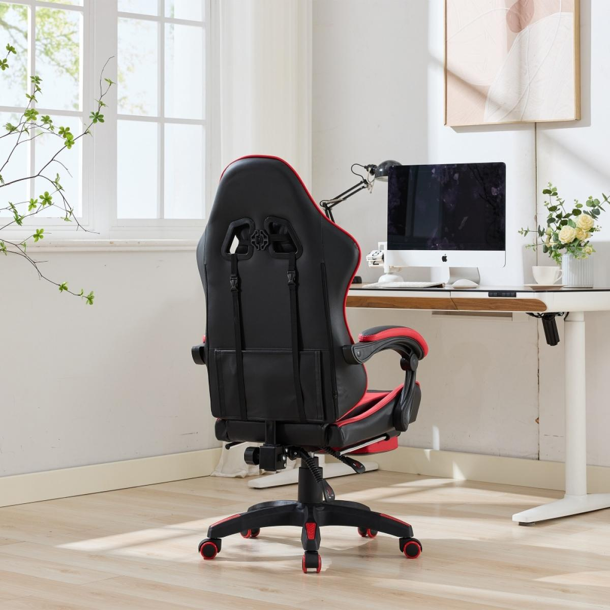Ein schwarzer und roter Gaming-Stuhl, der vom Betrachter weg zeigt, vor einem weißen Schreibtisch mit Computer und Fenster.