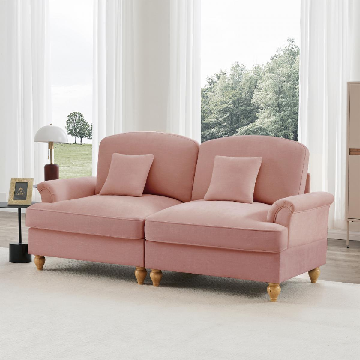 Ein rosa Sofa mit zwei Kissen steht in einem Raum mit einem Fenster. Eine Lampe und ein Bilderrahmen stehen auf einem Tisch.