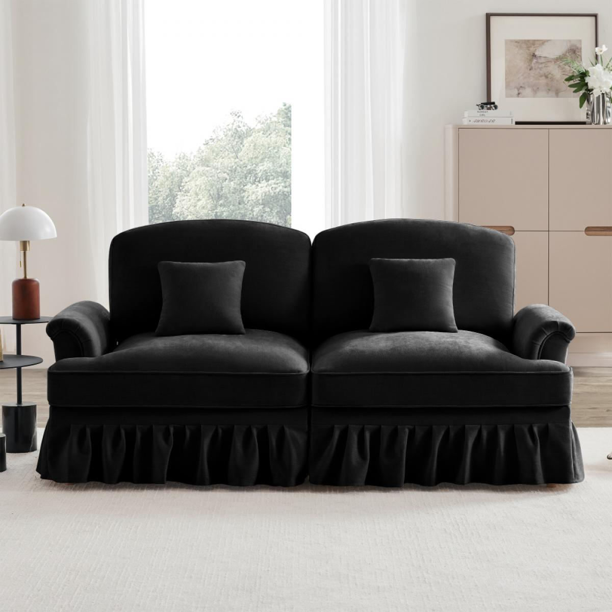 Ein schwarzes Sofa mit zwei Kissen steht vor einem Fenster. Auf der linken Seite steht ein Beistelltisch mit Lampe.