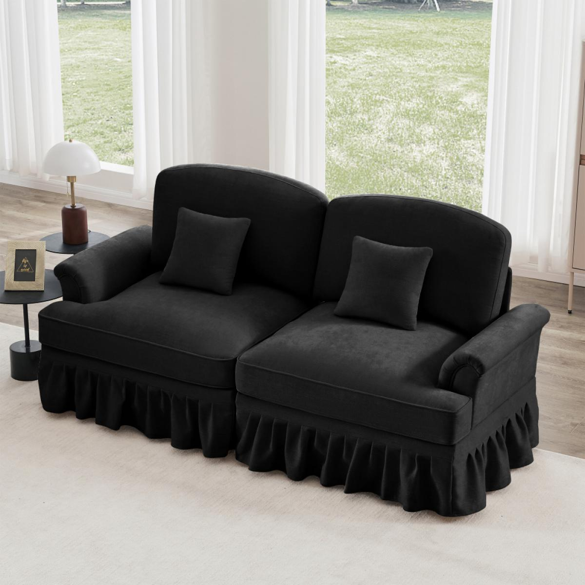 Ein schwarzes Sofa mit zwei Kissen steht auf einem hellen Teppich. Dahinter zeigt ein Fenster einen grünen Garten. Eine Lampe und ein Bilderrahmen sind zu sehen.