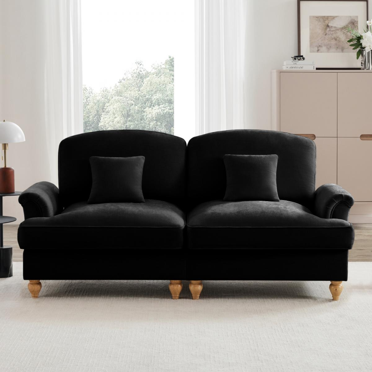 Ein schwarzes Sofa mit zwei Kissen steht auf einem weißen Teppich. Dahinter befinden sich ein Fenster mit weißen Vorhängen und ein Schrank.