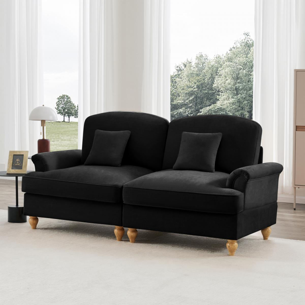 Ein schwarzes Sofa mit zwei Kissen steht auf einem weißen Teppich. Eine Lampe und ein gerahmtes Bild stehen auf einem Beistelltisch. Fenster und Bäume im Hintergrund.
