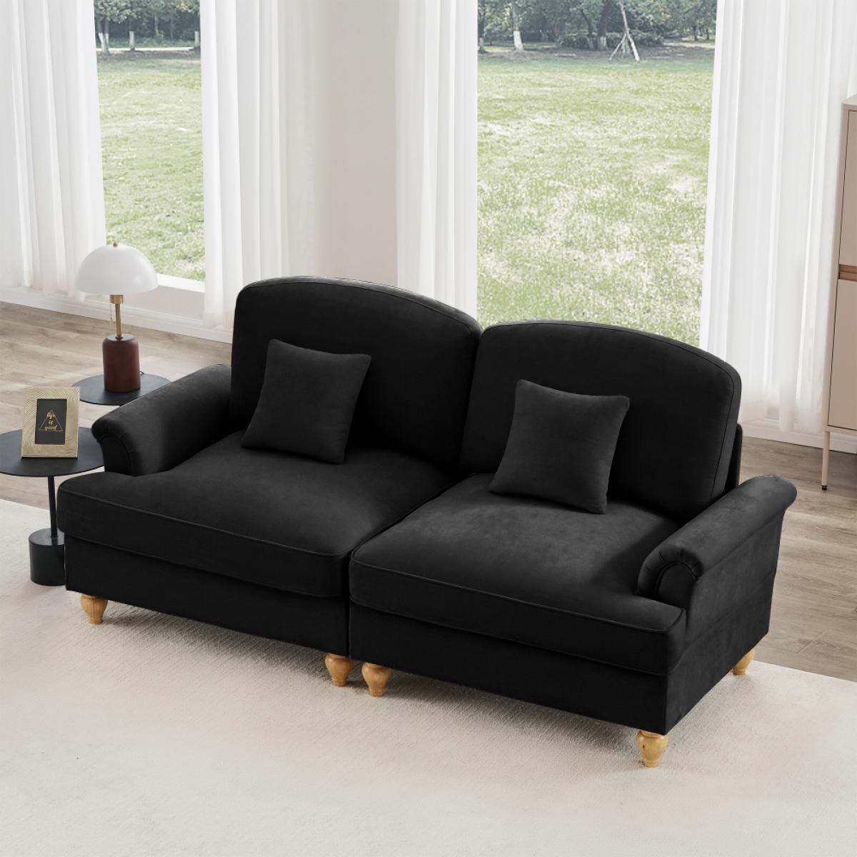 Ein schwarzes Sofa mit zwei Kissen steht auf einem weißen Teppich. Ein Beistelltisch mit Lampe und Fotorahmen links.