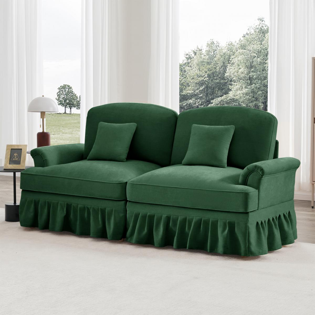 Ein grünes Sofa mit zwei Kissen und einem Rüschenrock steht auf einem weißen Teppich. Dahinter befindet sich ein Fenster mit Bäumen und weißen Vorhängen.