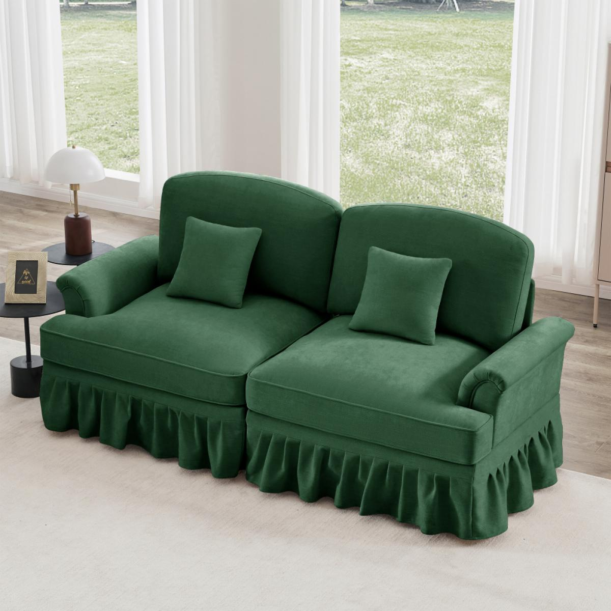 Ein grünes Sofa mit zwei Abschnitten, zwei Kissen und Rüschenrock, vor einem Fenster mit weißen Vorhängen und Gartenblick.