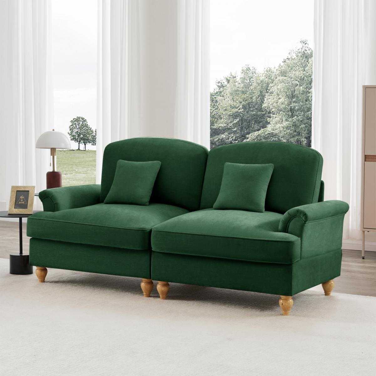 Ein grünes Sofa mit zwei Kissen steht in einem Raum mit Fenster und weißen Vorhängen. Daneben steht ein kleiner Tisch mit einer Lampe.