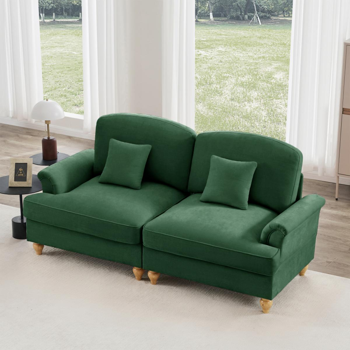 Ein grünes Sofa mit zwei Kissen steht auf einem weißen Teppich. Dahinter befinden sich Fenster mit weißen Vorhängen und Blick ins Grüne.